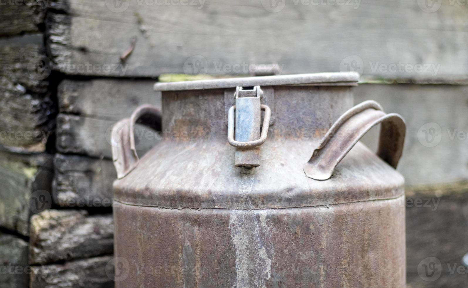 One old rusty metal can in the countryside. Container for transporting liquids, milk or liquid fuels with multiple handles. Milk bank of a cylindrical form with a wide mouth. Bottle with sealed cap. photo