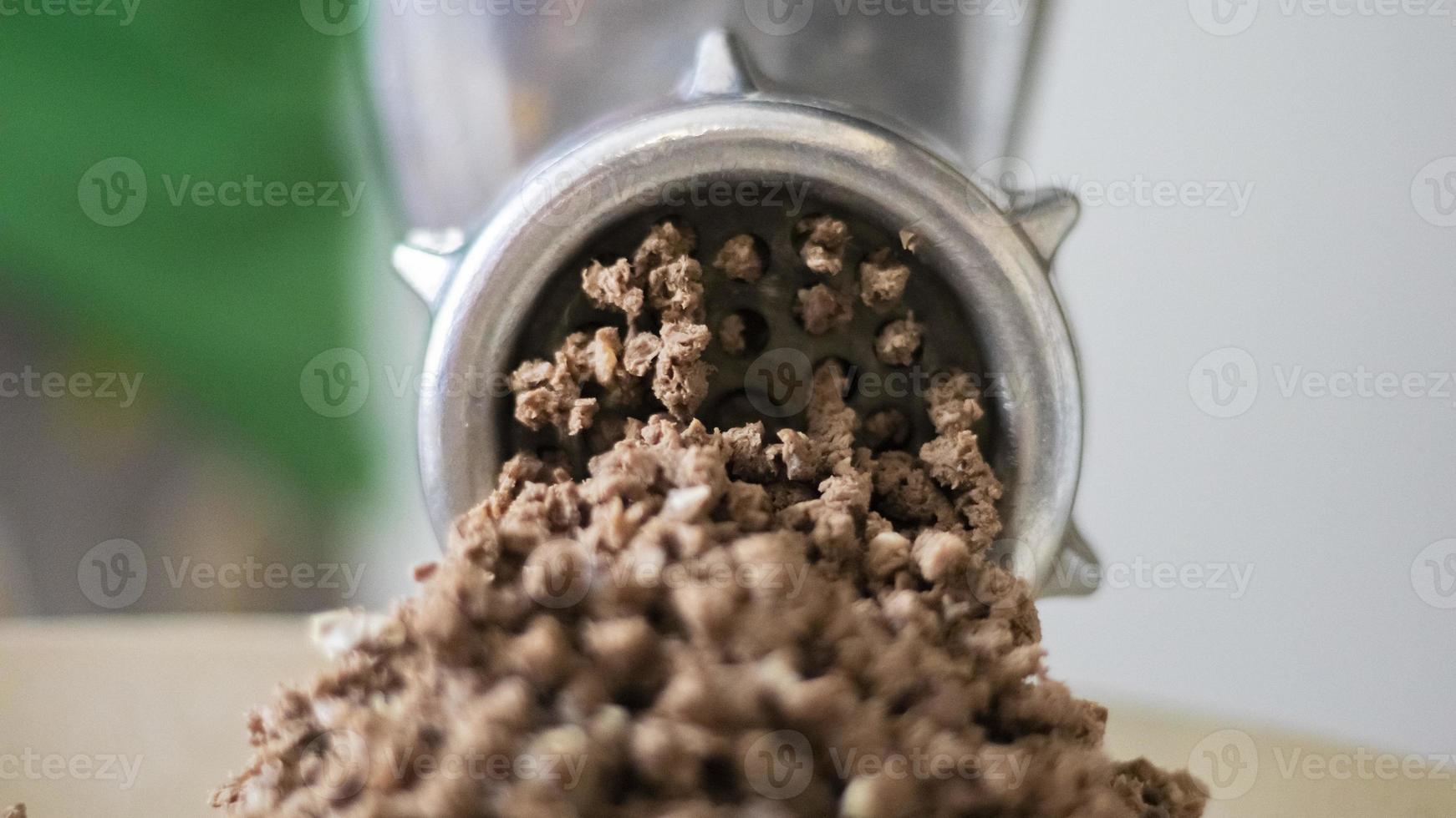 Minced meat in a manual mechanical meat grinder. Fresh boiled meat is ground with an old metal meat grinder, close-up in the kitchen. photo