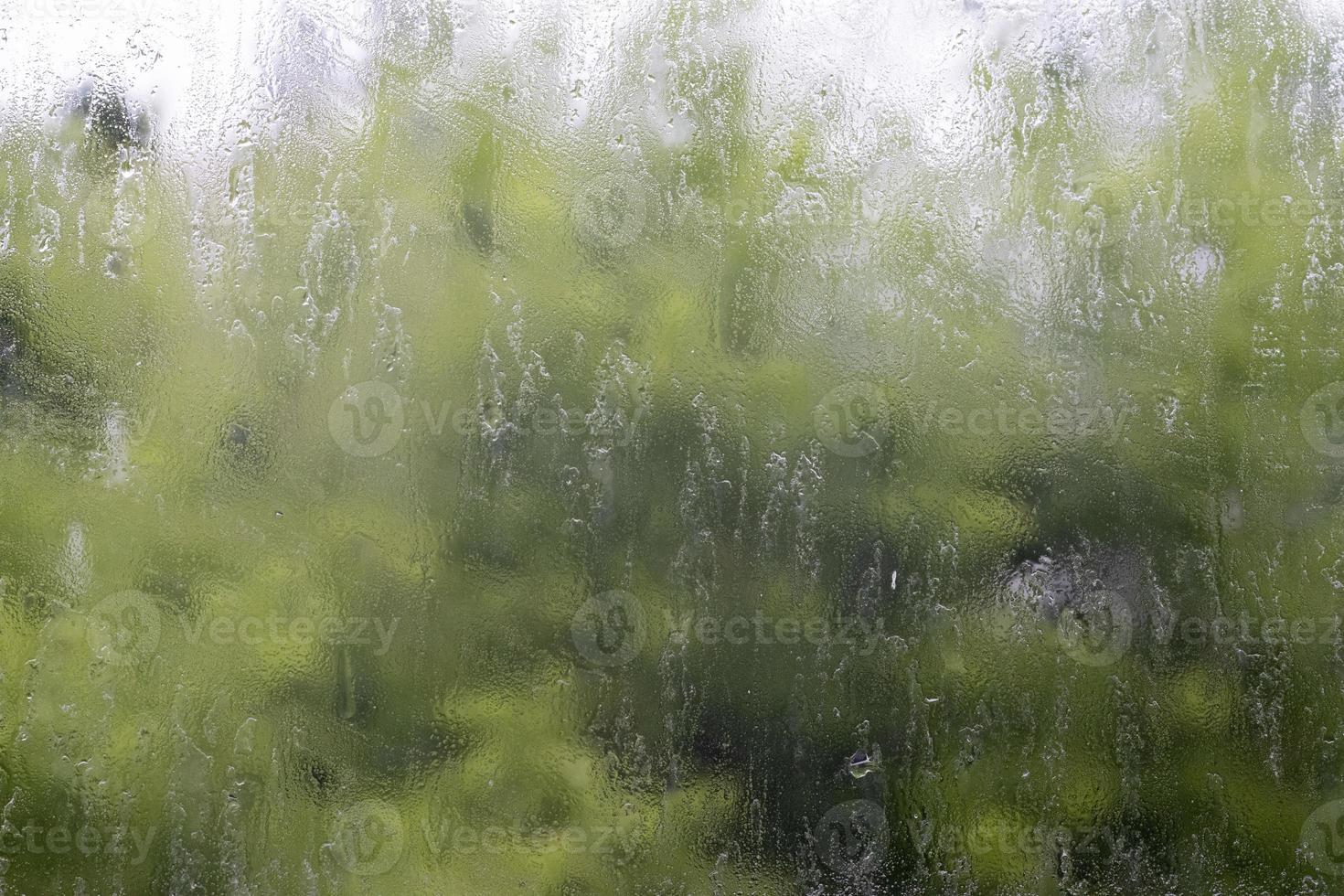 Heavy rain. Raindrops on the window glass on a summer day. Selective focus, shallow depth of field. Drops of water fall on a wet window. Glass full of drops during a downpour. photo