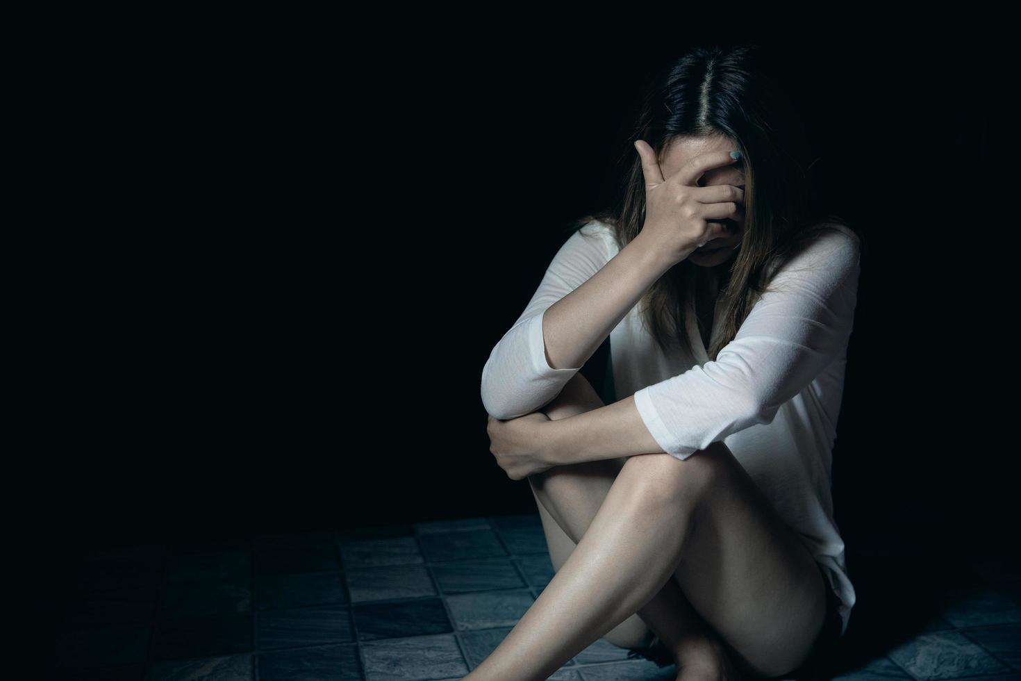 mujer joven triste, estresada y solitaria sentada en una habitación oscura, adolescente infeliz y llorando por violencia doméstica, una mujer adulta expresa sentimientos de desesperación, ansiedad por el acoso. foto