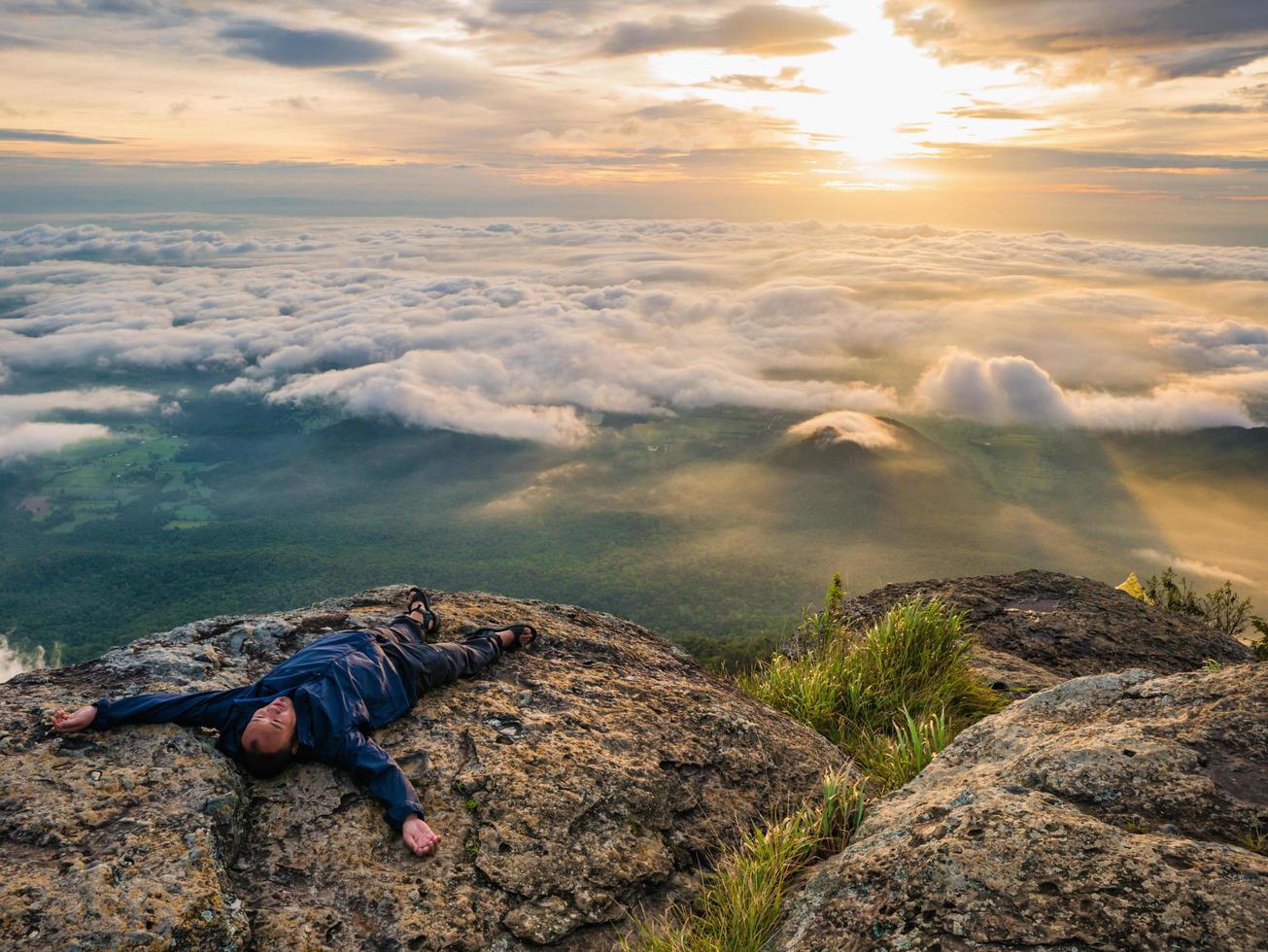 trekker se acostó en el acantilado con un hermoso amanecer y un mar de niebla por la mañana en la montaña khao luang en el parque nacional ramkhamhaeng, provincia de sukhothai, tailandia foto