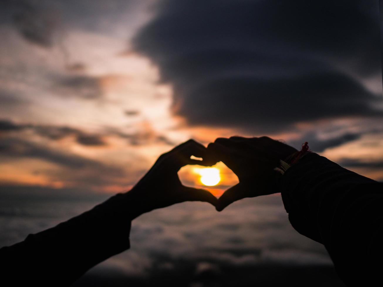 silueta, corazón, mano, señal, con, salida del sol, en, el, montaña foto