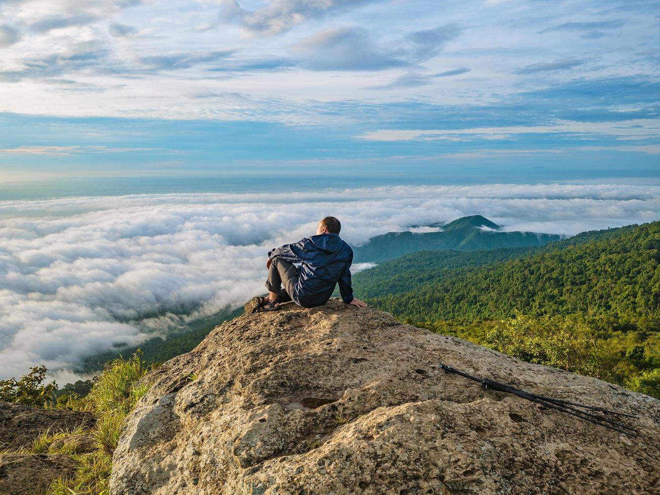 los hombres asiáticos se sientan en el acantilado con el hermoso cielo del amanecer en la montaña khao luang en el parque nacional ramkhamhaeng, provincia de sukhothai, tailandia foto