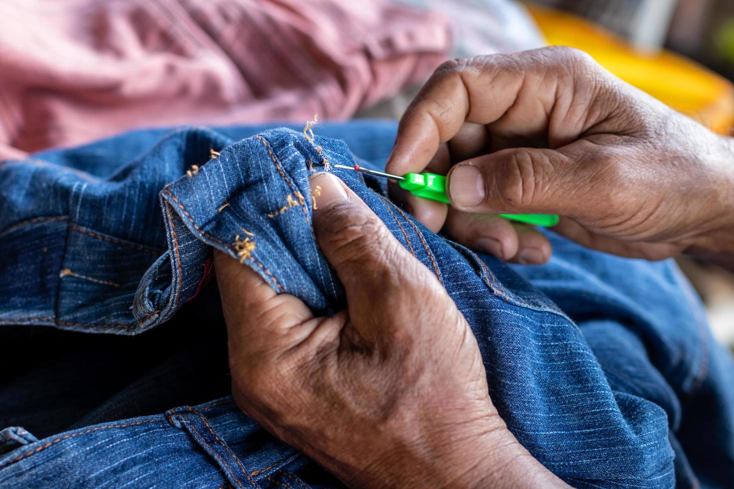 Close-up view of both hands of an elderly Thai man using a needle to pick up threads to repair jeans. photo