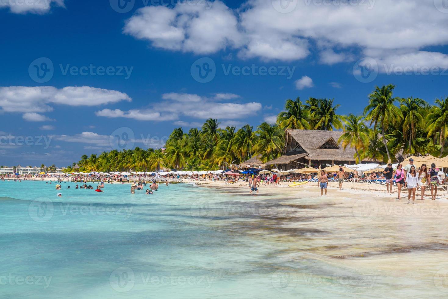 People swimming near white sand beach with umbrellas, bungalow bar and cocos palms, turquoise caribbean sea, Isla Mujeres island, Caribbean Sea, Cancun, Yucatan, Mexico photo