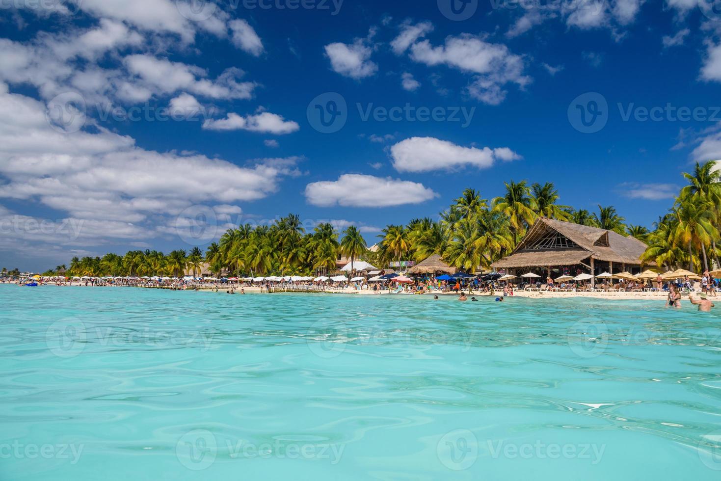 People swimming near white sand beach with umbrellas, bungalow bar and cocos palms, turquoise caribbean sea, Isla Mujeres island, Caribbean Sea, Cancun, Yucatan, Mexico photo