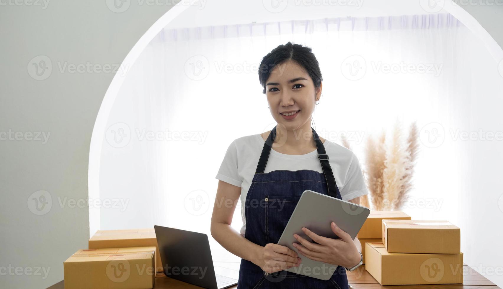 Startup SME small business entrepreneur SME or freelance Asian woman using a laptop with box, Young success Asian woman with her hand lift up, online marketing packaging box and delivery, SME concept. photo