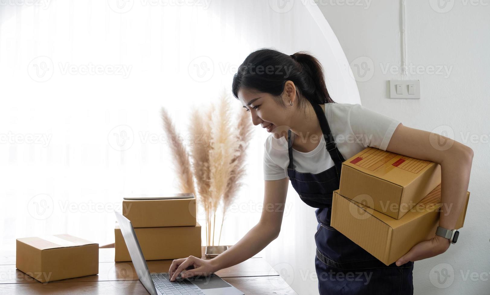 Startup happy Asian woman business owner works with a box at home, prepare parcel delivery SME supply chain, procurement, package box to deliver to customers, Online SME business entrepreneurs ideas, photo