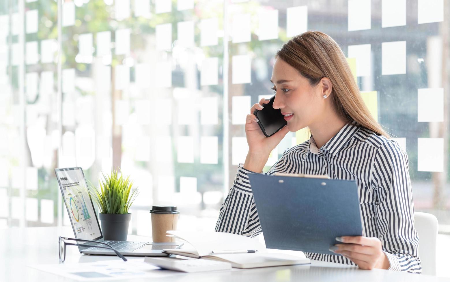 Portrait of young asian business woman talk on smartphone write notebook laptop in home office. Beautiful girl at desk computer take home order. Startup business asia woman online sme telemarketing. photo