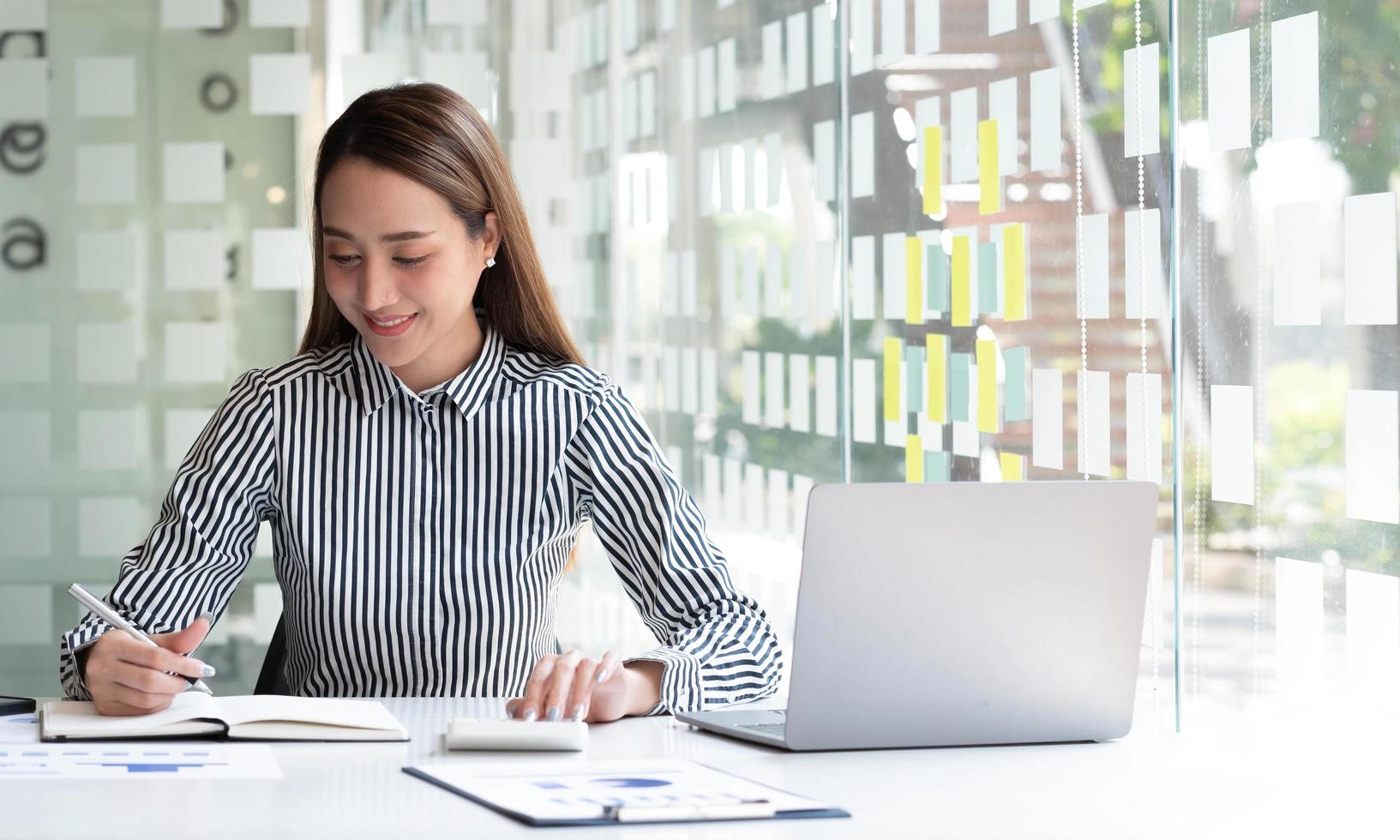 Beautiful Asian businesswoman analyzes charts using laptop calculator at the office. photo