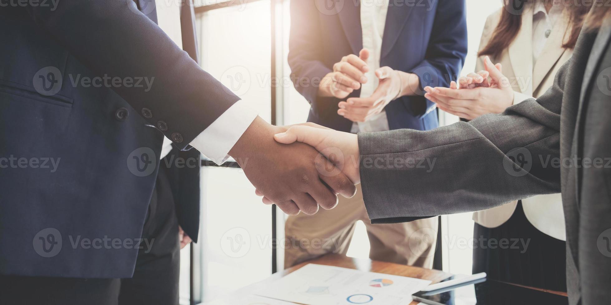 Two  business men shaking hands while their colleagues applauding in the background photo