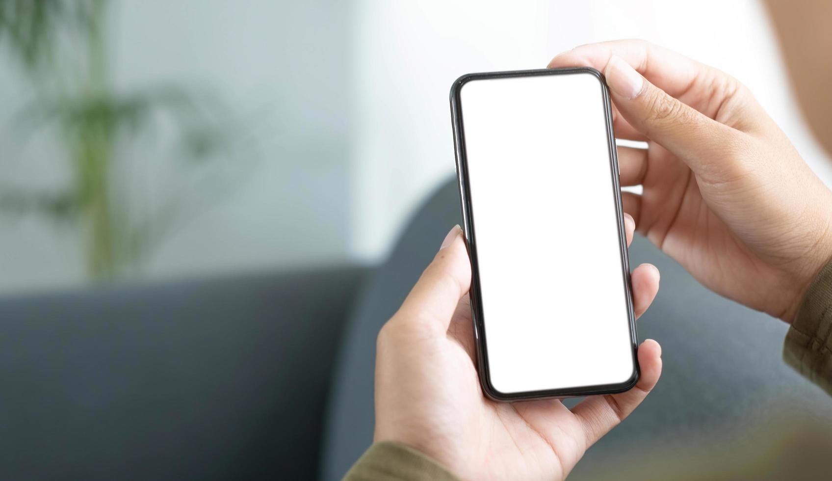 imagen de maqueta de teléfono celular de pantalla blanca en blanco. Mano de mujer sosteniendo mensajes de texto usando el móvil en el sofá foto