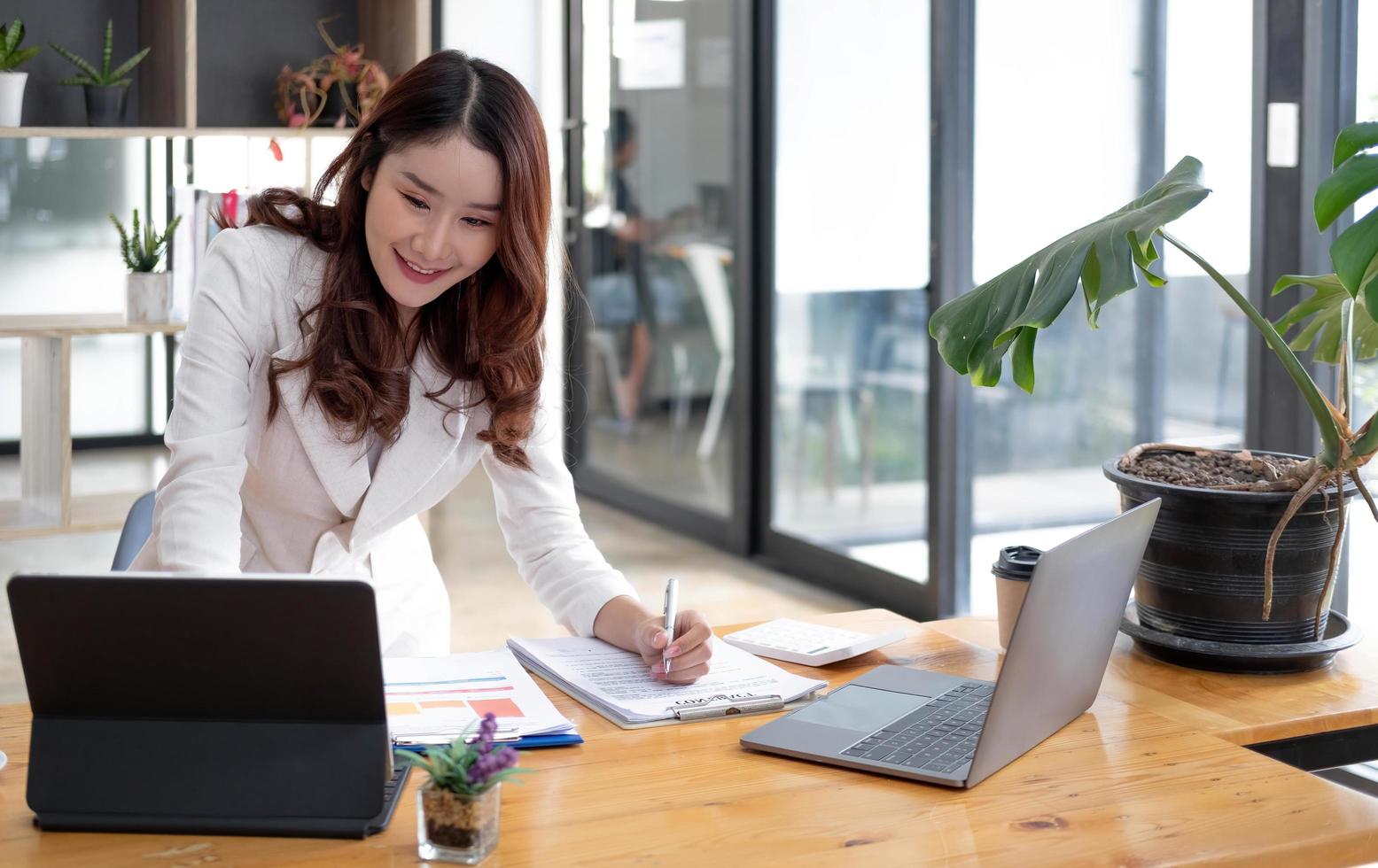 Happy young Asian businesswoman standing using laptop computer at office. photo