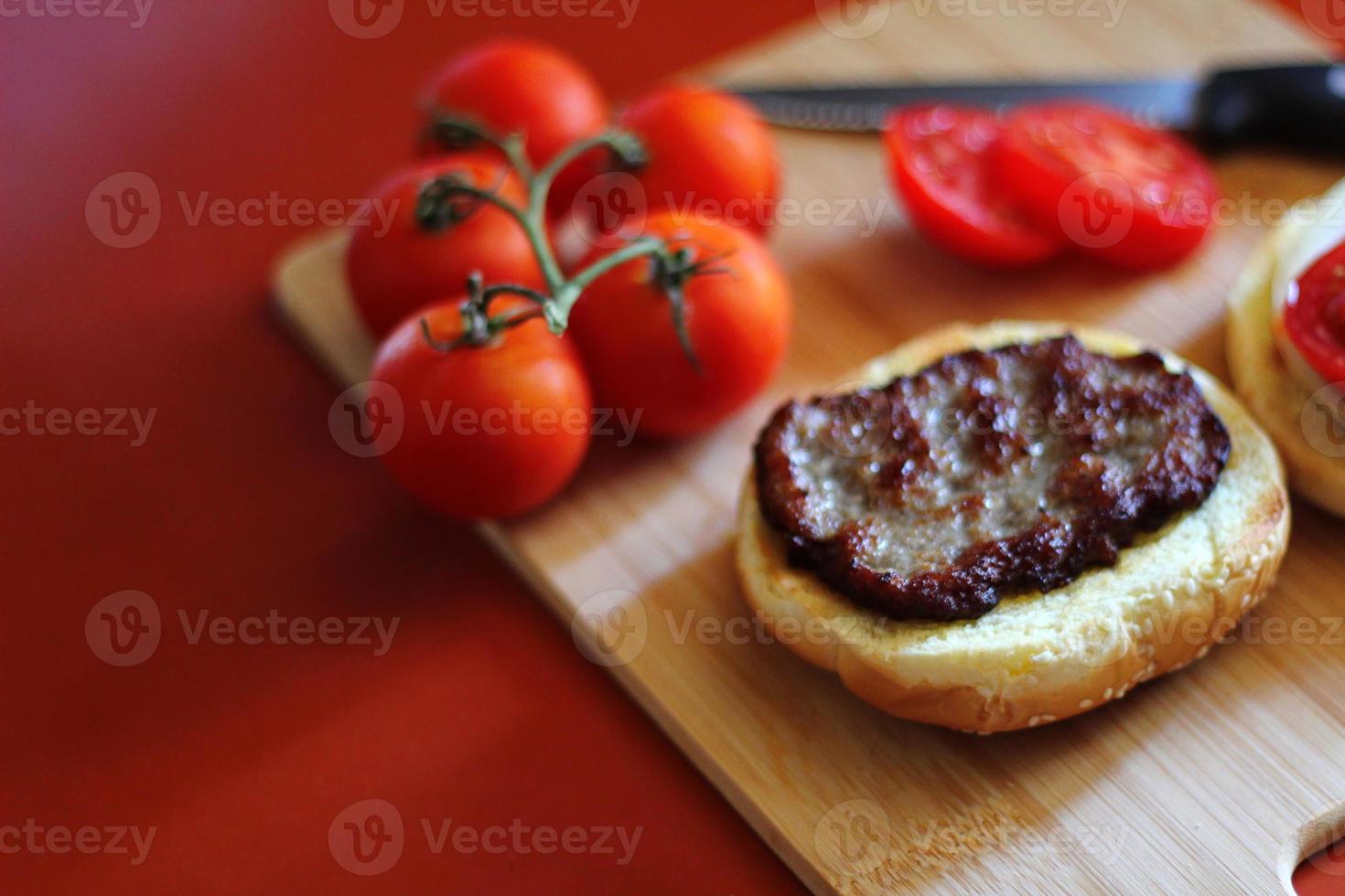 The hamburger is being prepared and served with sliced tomatoes, onions, pickles. on a wooden cutting board in the kitchen photo