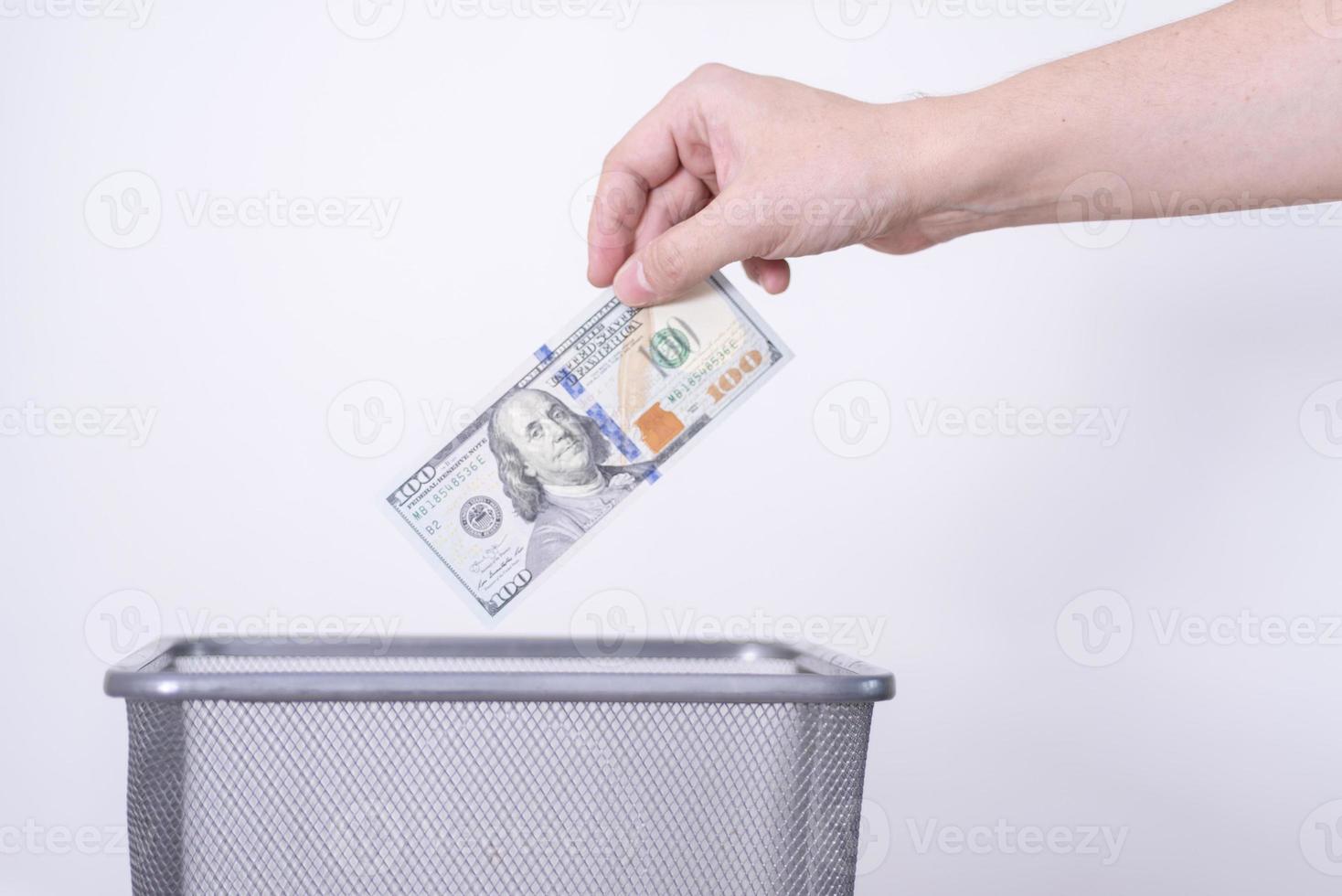 A hand throws dollar bills into a trash can against a gray background. photo