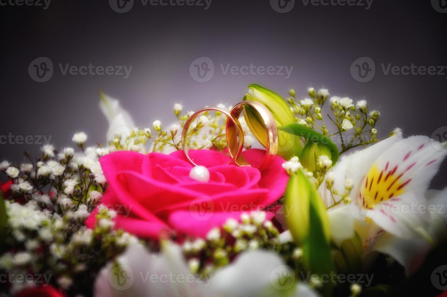 Golden wedding ring with pink roses and white lilies close-up photo