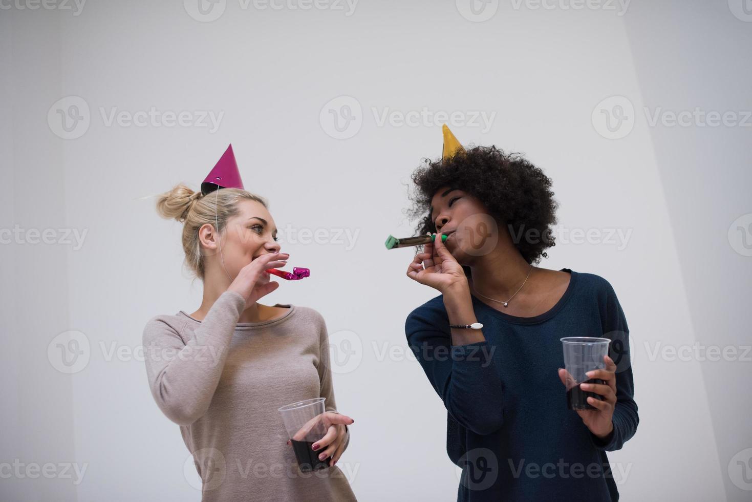 mujeres sonrientes con gorras de fiesta que soplan silbatos foto