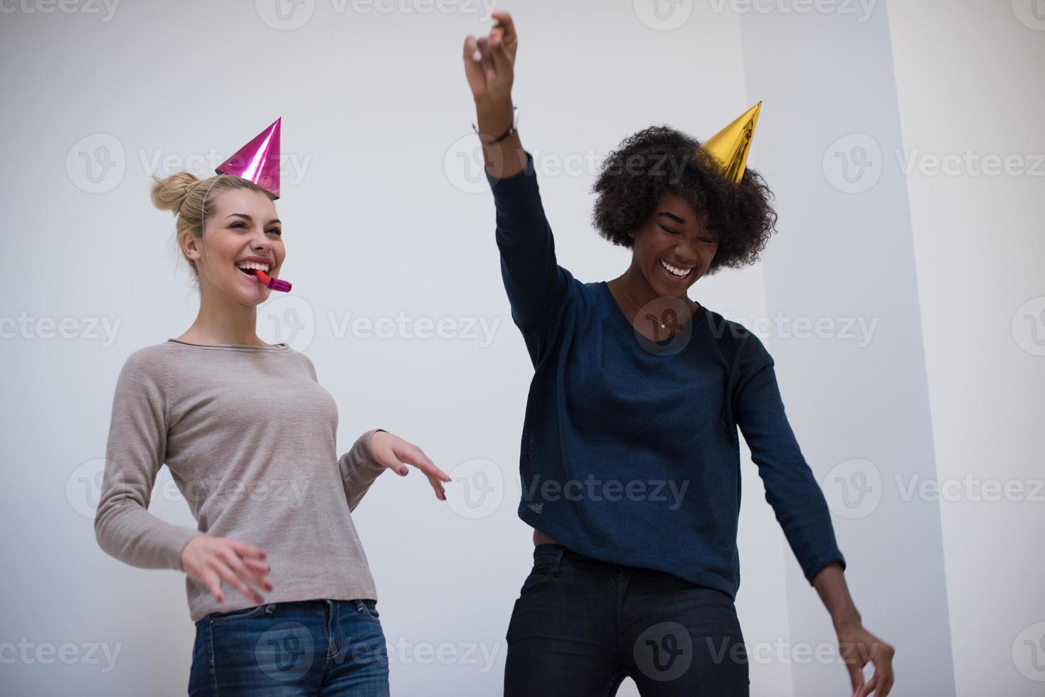 mujeres sonrientes con gorras de fiesta que soplan silbatos foto