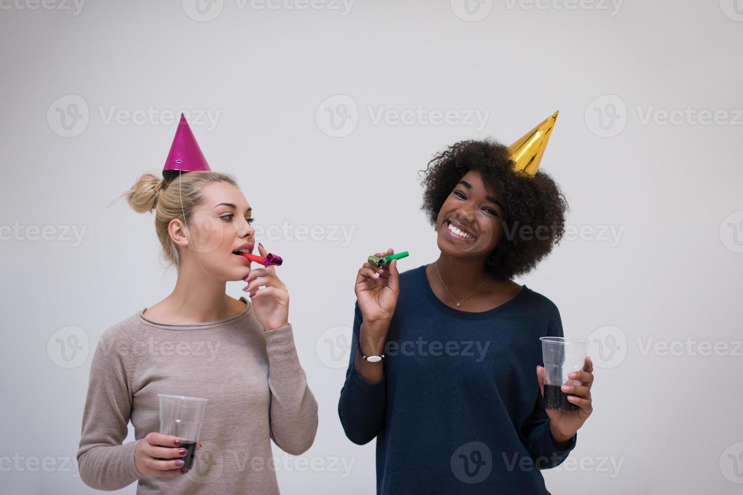 mujeres sonrientes con gorras de fiesta que soplan silbatos foto