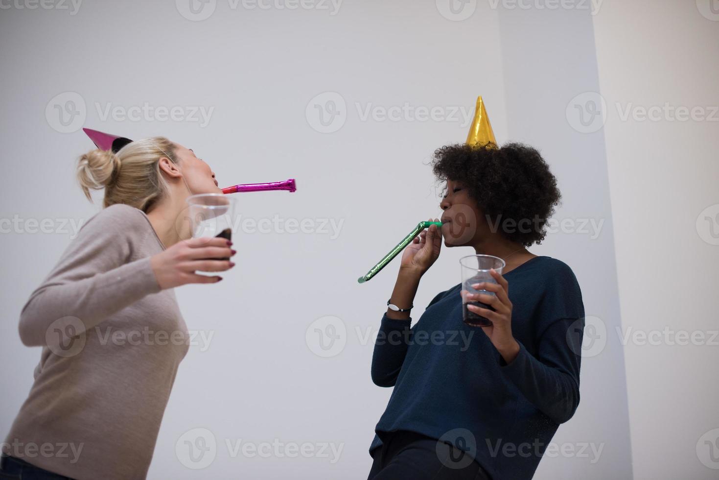 smiling women in party caps blowing to whistles photo