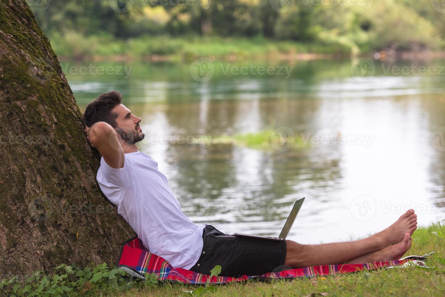 man using a laptop computer on the bank of the river photo