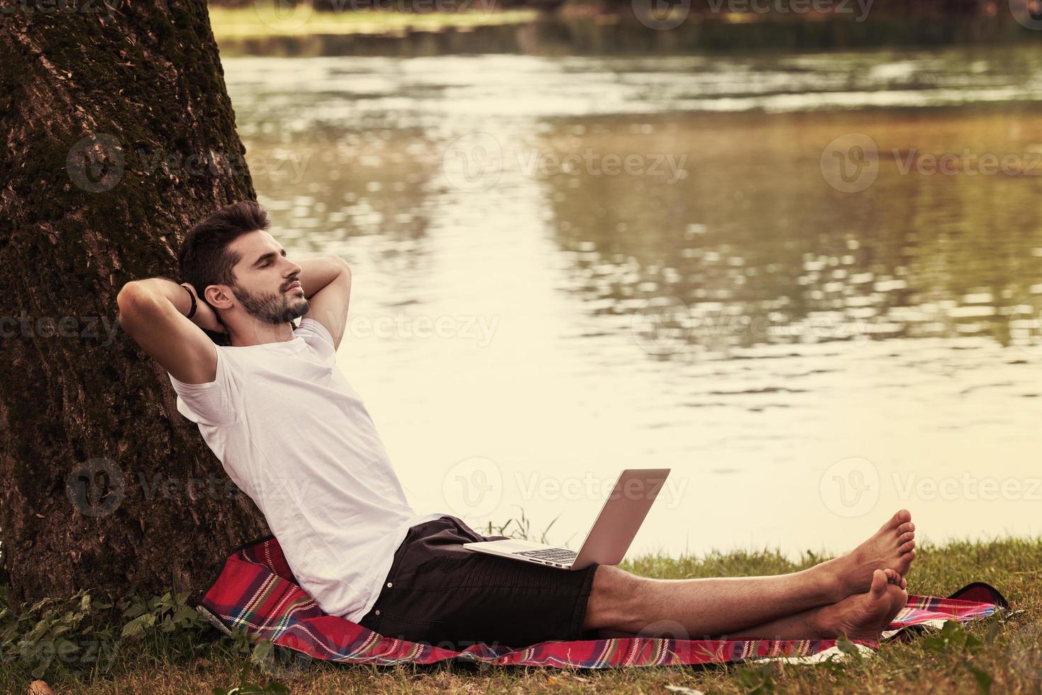 man using a laptop computer on the bank of the river photo