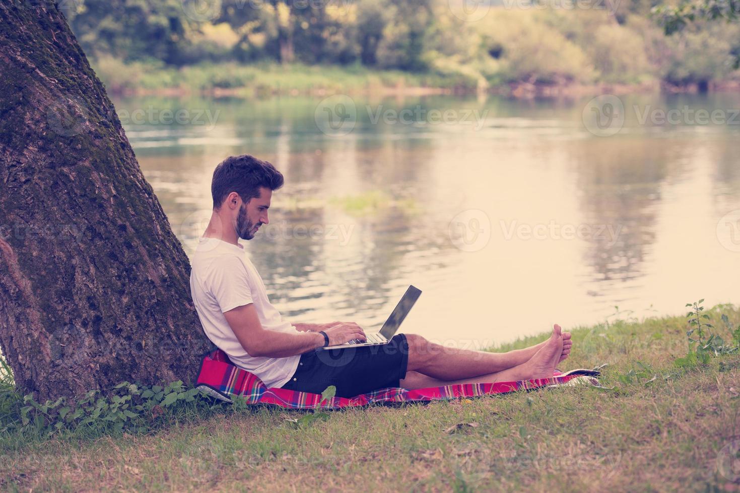 man using a laptop computer on the bank of the river photo