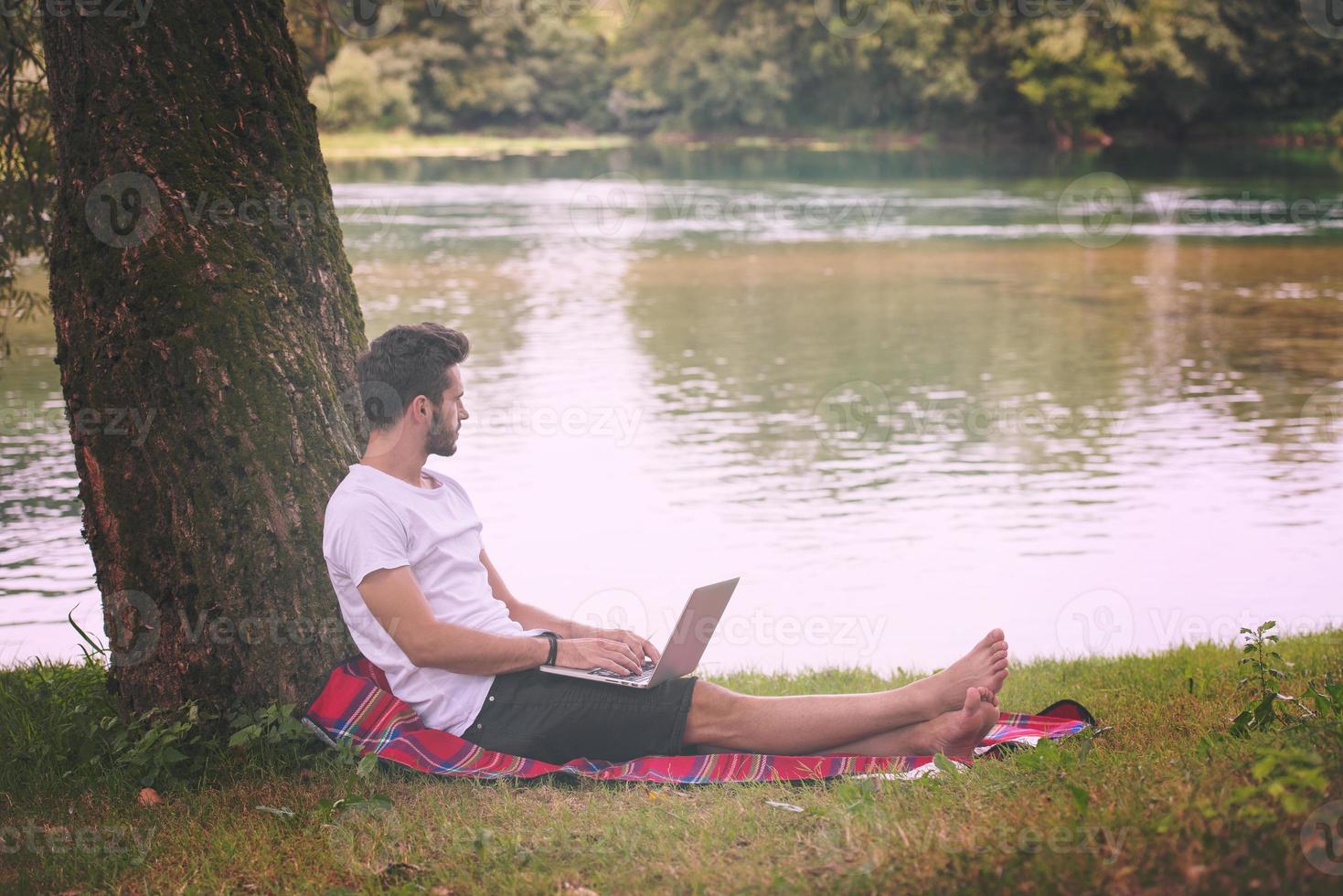 man using a laptop computer on the bank of the river photo