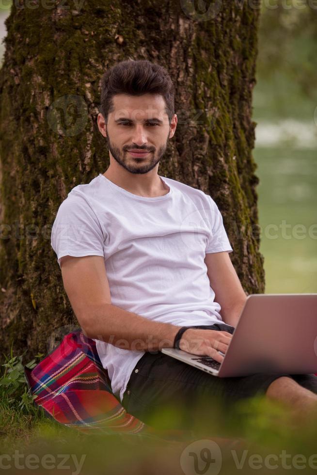 man using a laptop computer on the bank of the river photo