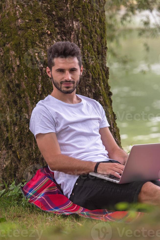 man using a laptop computer on the bank of the river photo