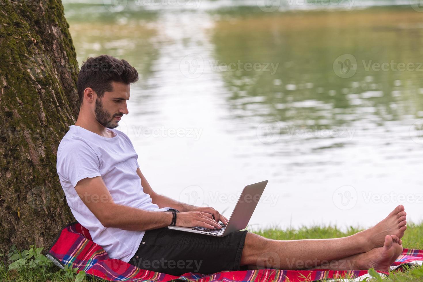 man using a laptop computer on the bank of the river photo