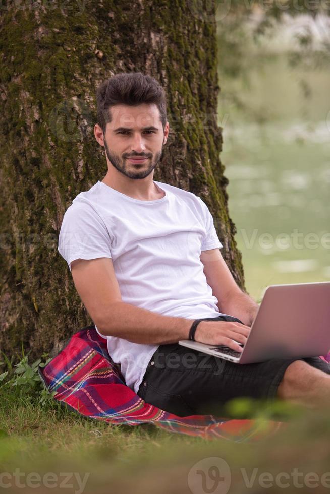 man using a laptop computer on the bank of the river photo