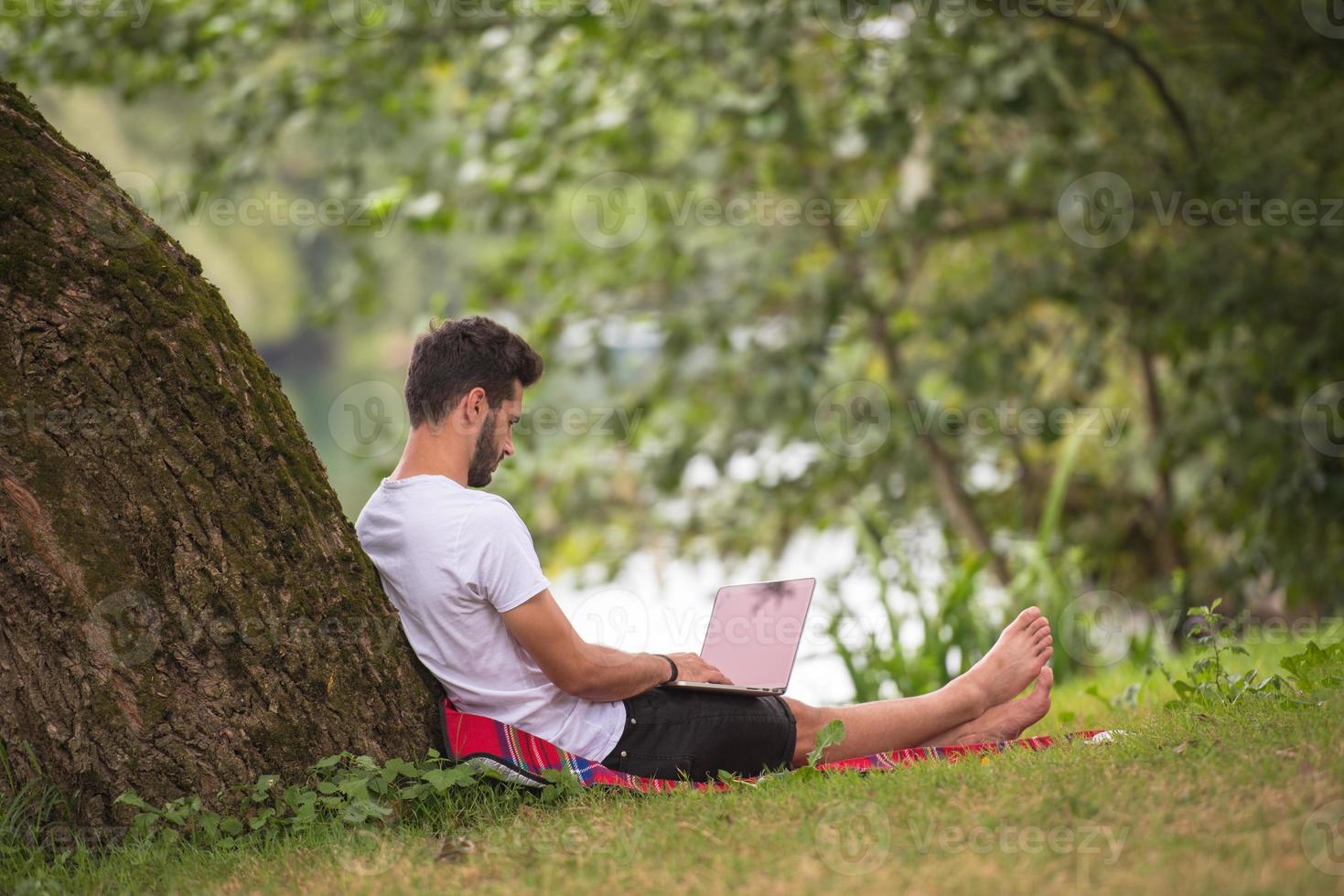 man using a laptop computer on the bank of the river photo