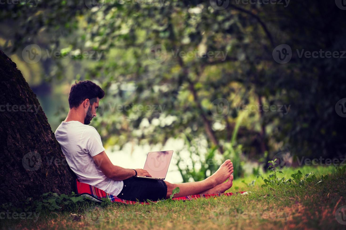 man using a laptop computer on the bank of the river photo