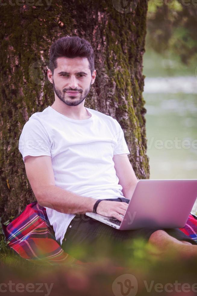 man using a laptop computer on the bank of the river photo