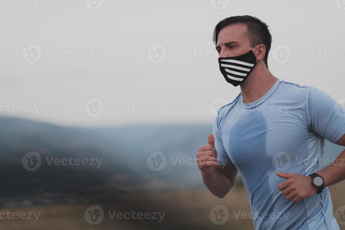 hombre de fitness con ropa deportiva mojada con mascarilla protectora negra corriendo al aire libre en la ciudad durante el brote de coronavirus. covid 19 y actividad física de jogging deporte y fitness. nueva normalidad foto