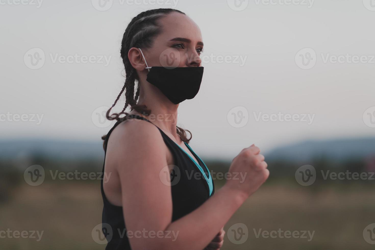 Determined fitness woman in short clothes wearing red protective face mask running outdoors in the city during coronavirus outbreak. Covid 19 and physical jogging activity, sport and fitness. photo