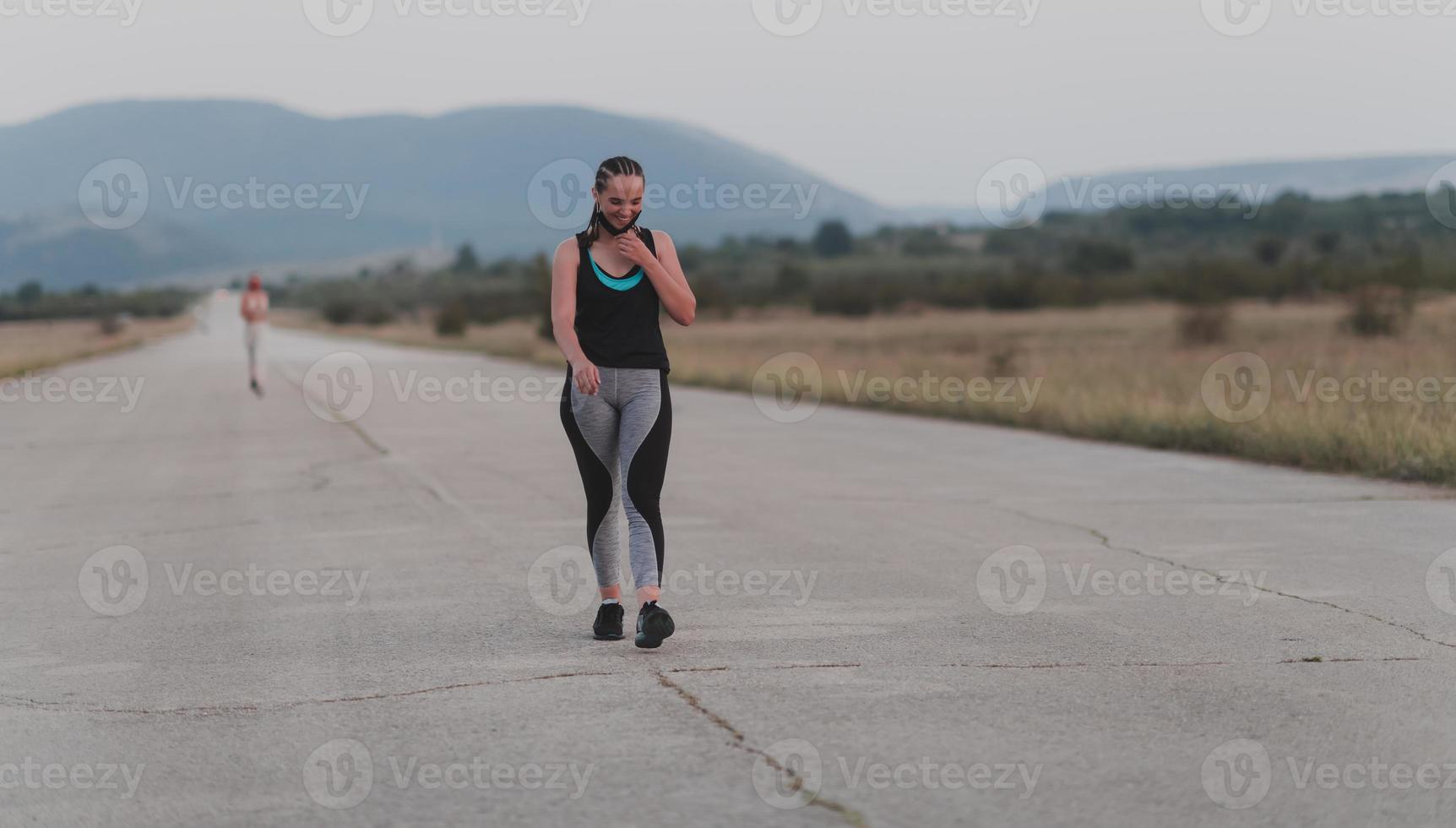 Determined fitness woman in short clothes wearing red protective face mask running outdoors in the city during coronavirus outbreak. Covid 19 and physical jogging activity, sport and fitness. photo