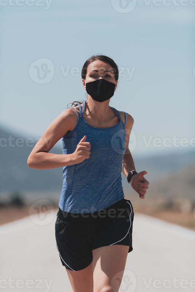 determinada mujer fitness con ropa corta y mascarilla protectora roja corriendo al aire libre en la ciudad durante el brote de coronavirus. covid 19 y actividad física de jogging, deporte y fitness. foto