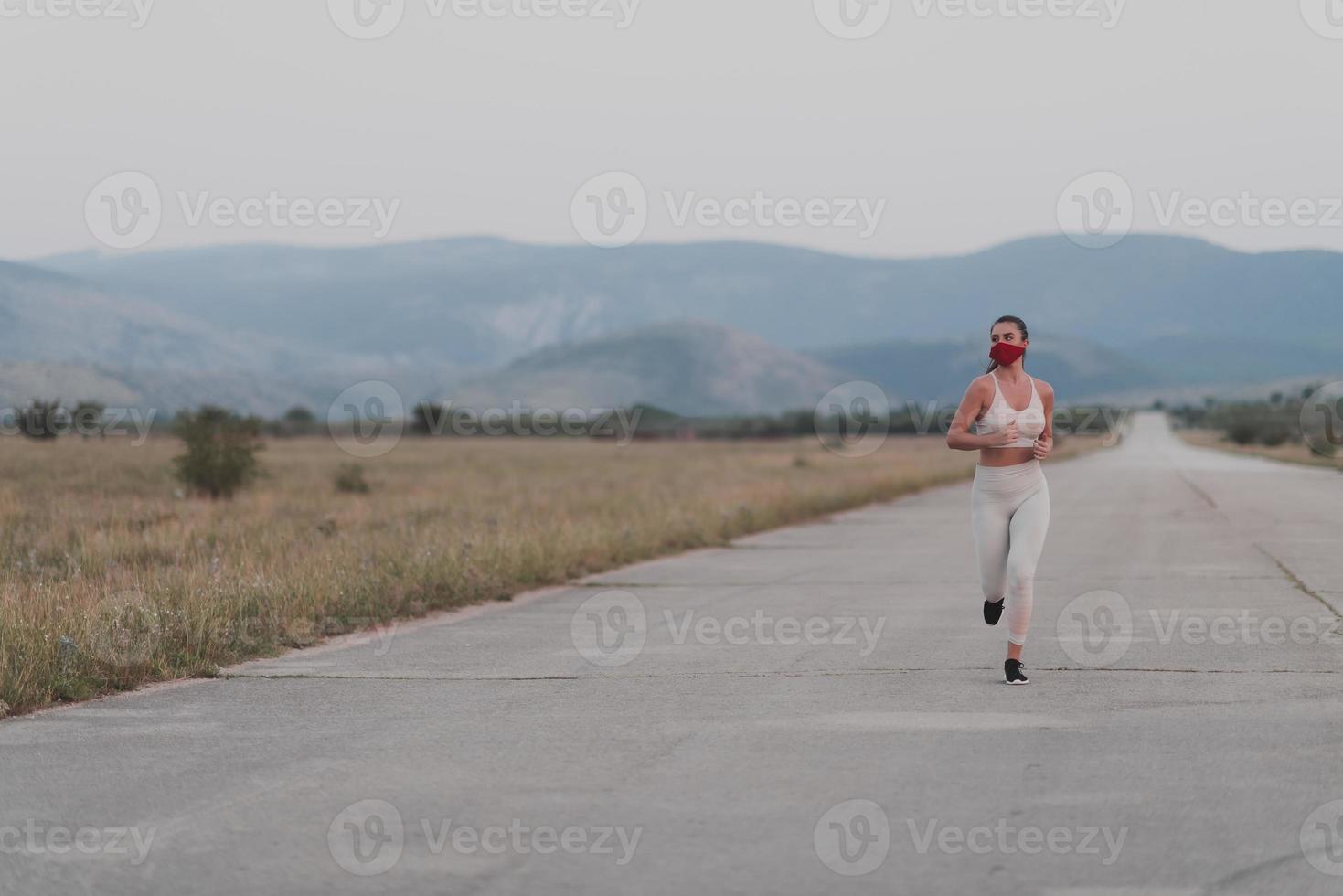 determinada mujer fitness con ropa corta y mascarilla protectora roja corriendo al aire libre en la ciudad durante el brote de coronavirus. covid 19 y actividad física de jogging deporte y fitness. foto