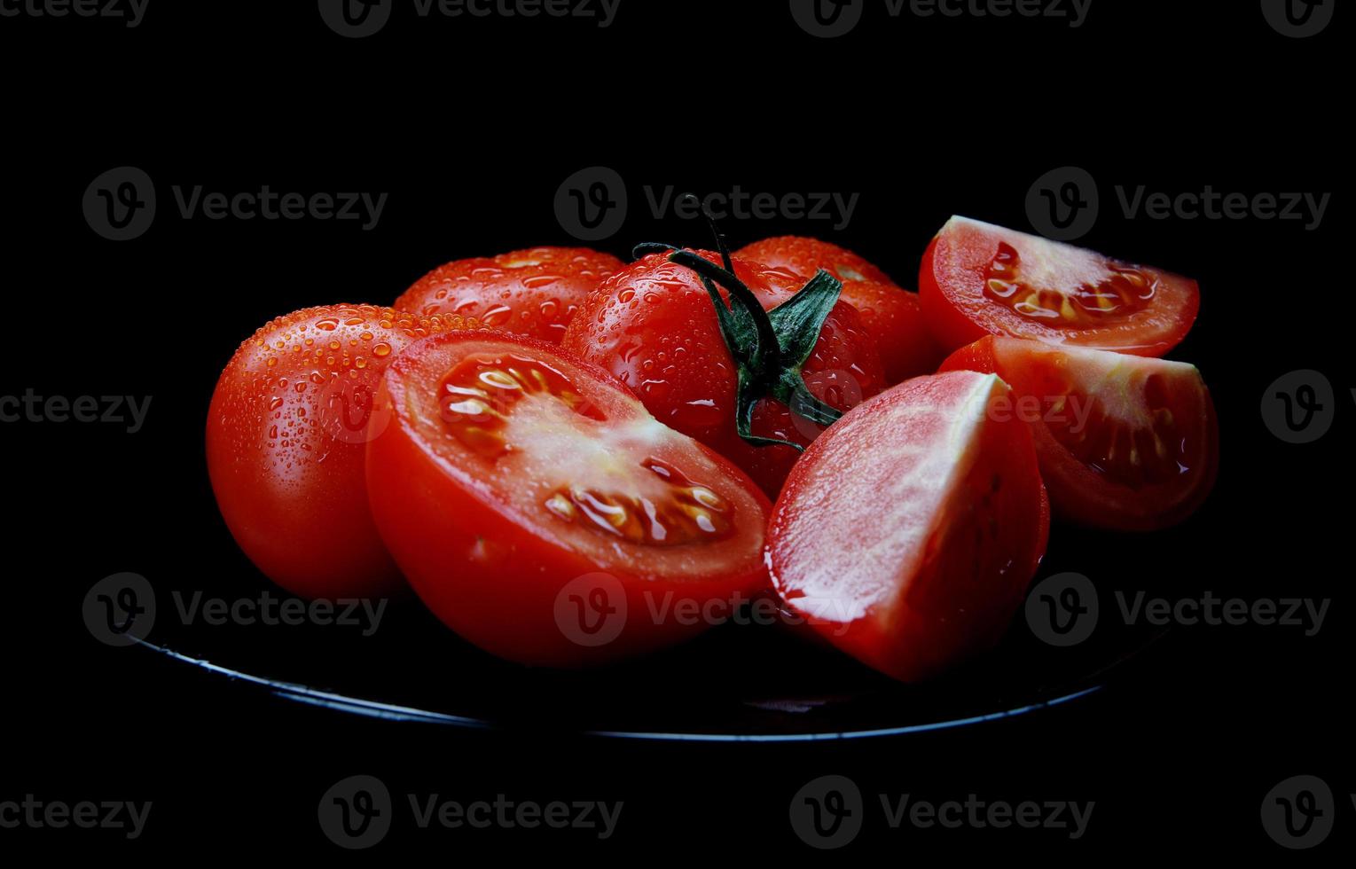 los tomates rojos en rodajas en un plato negro están aislados en un fondo negro. camino de recortes foto