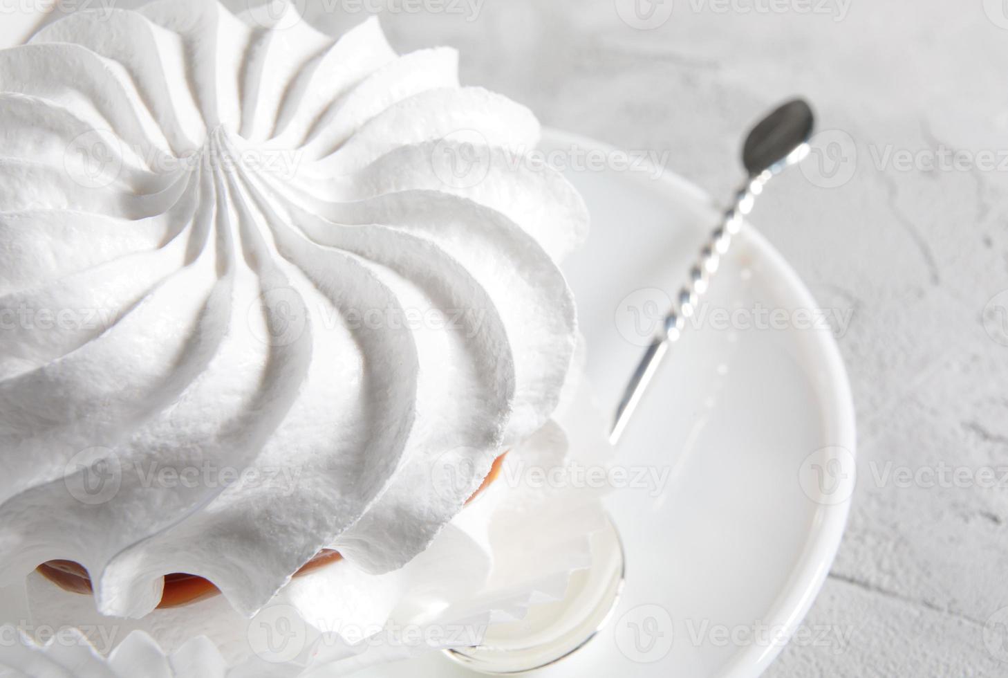 Beautiful white meringues with a silver spoon on a white plate. White cake. photo