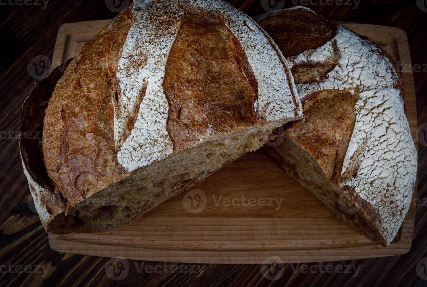 una hogaza de pan de centeno cortada por la mitad en una tabla de cortar de madera. pan casero. foto