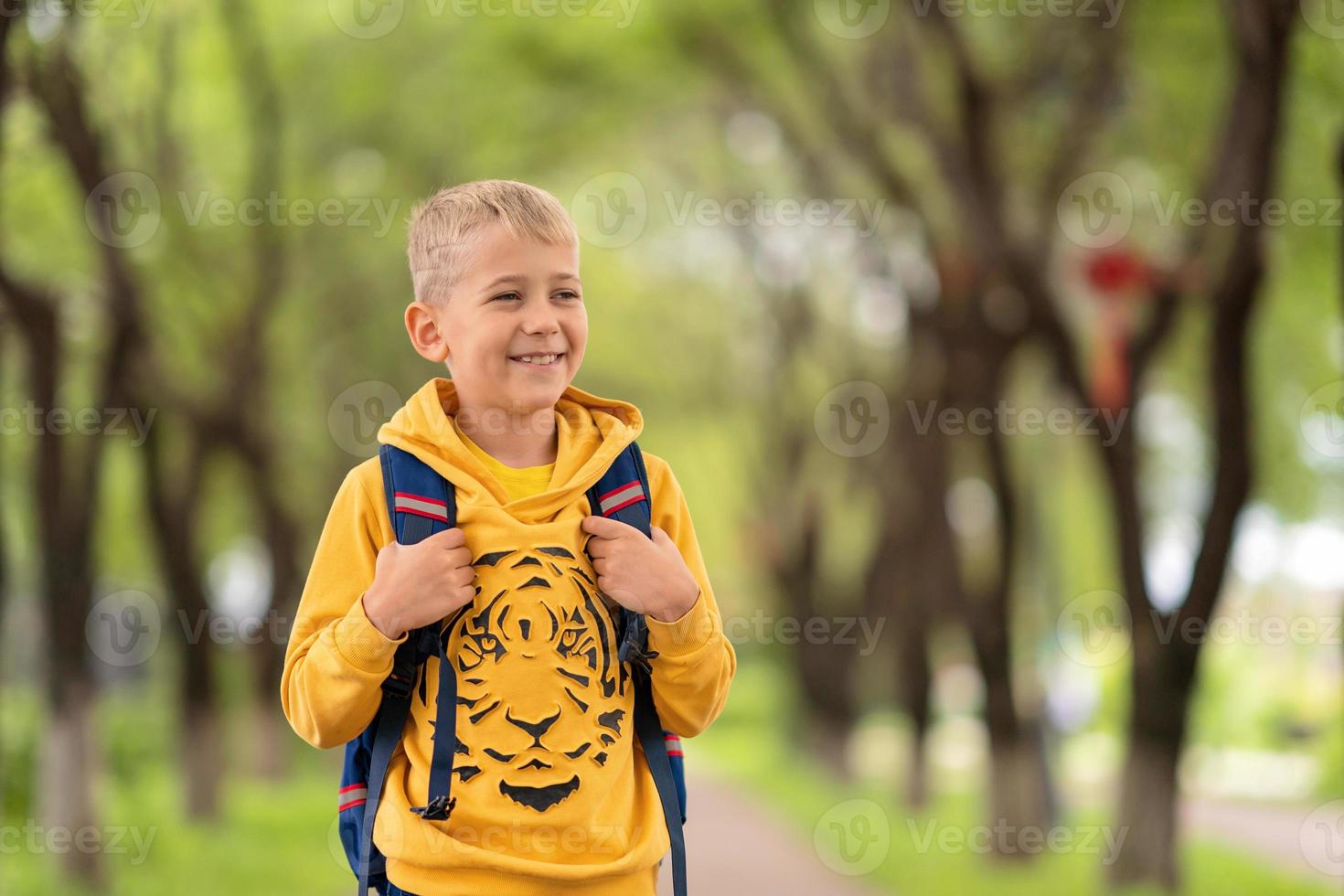 un chico rubio con una sudadera amarilla y una mochila sobre los hombros yendo a la escuela foto