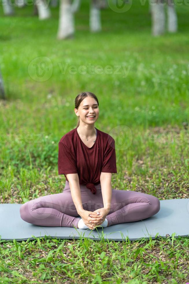 Young girl having online workout outdoors using laptop. Pilates or yoga video lesson on internet. Happy smiling girl practicing pilates lesson online in garden outdoors during quarantine. photo