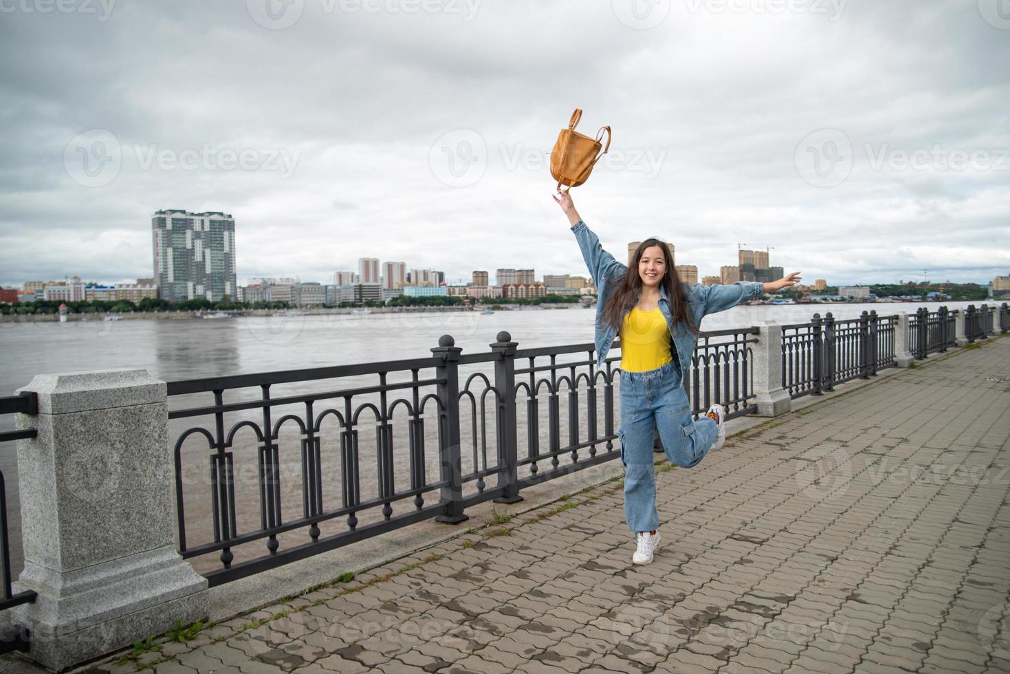 Happy girl in a denim wear jumping with backpack in her hand photo