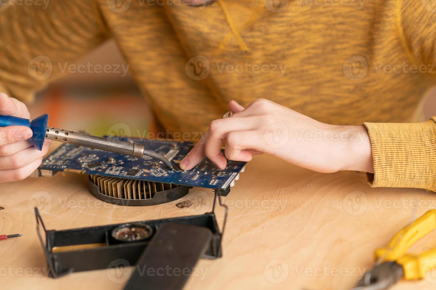 a young man solders a burnt-out microcircuit with a soldering iron photo