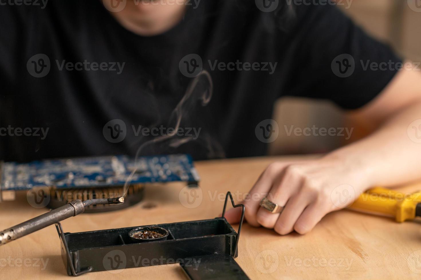 a young man solders a burnt-out microcircuit with a soldering iron photo