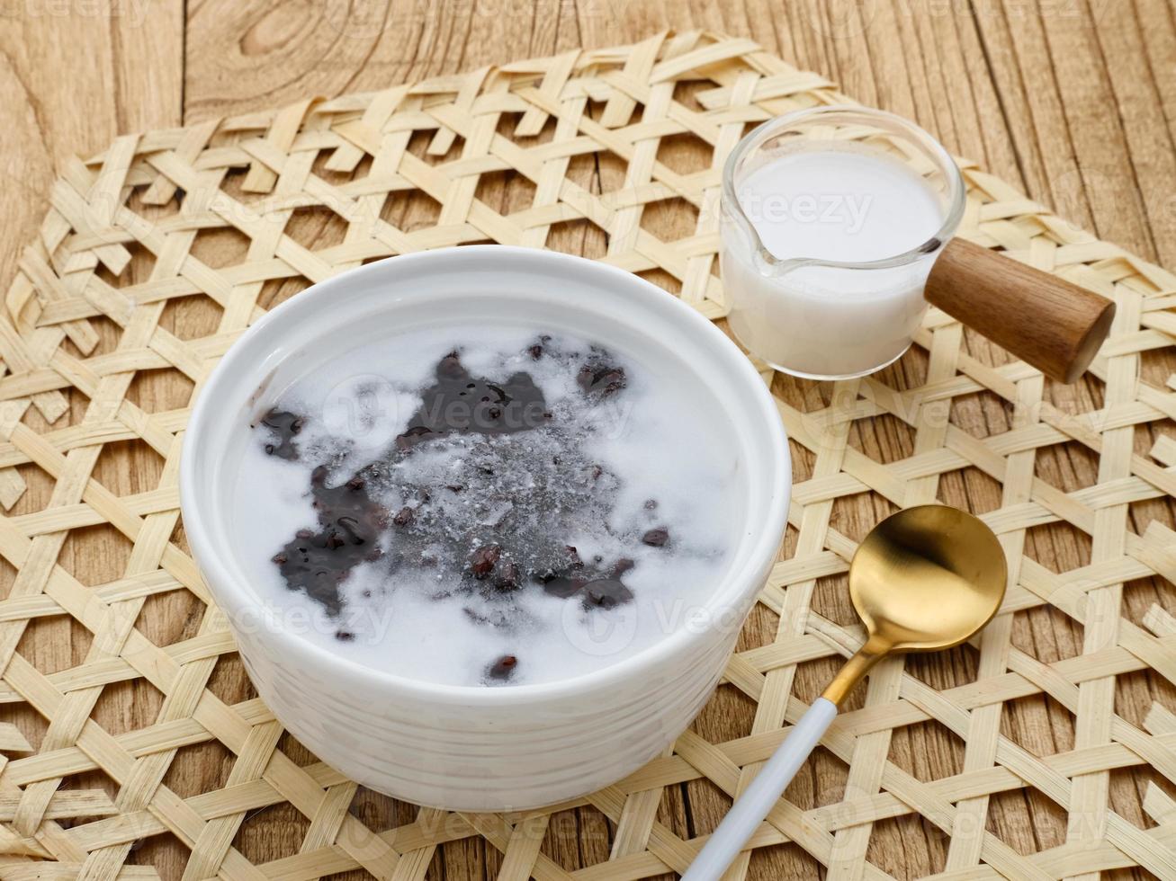 Bubur Ketan Hitam, Indonesian dessert. Black glutinous rice porridge with coconut milk, sugar and pandan leaf. Served in a white bowl on a wooden table. photo