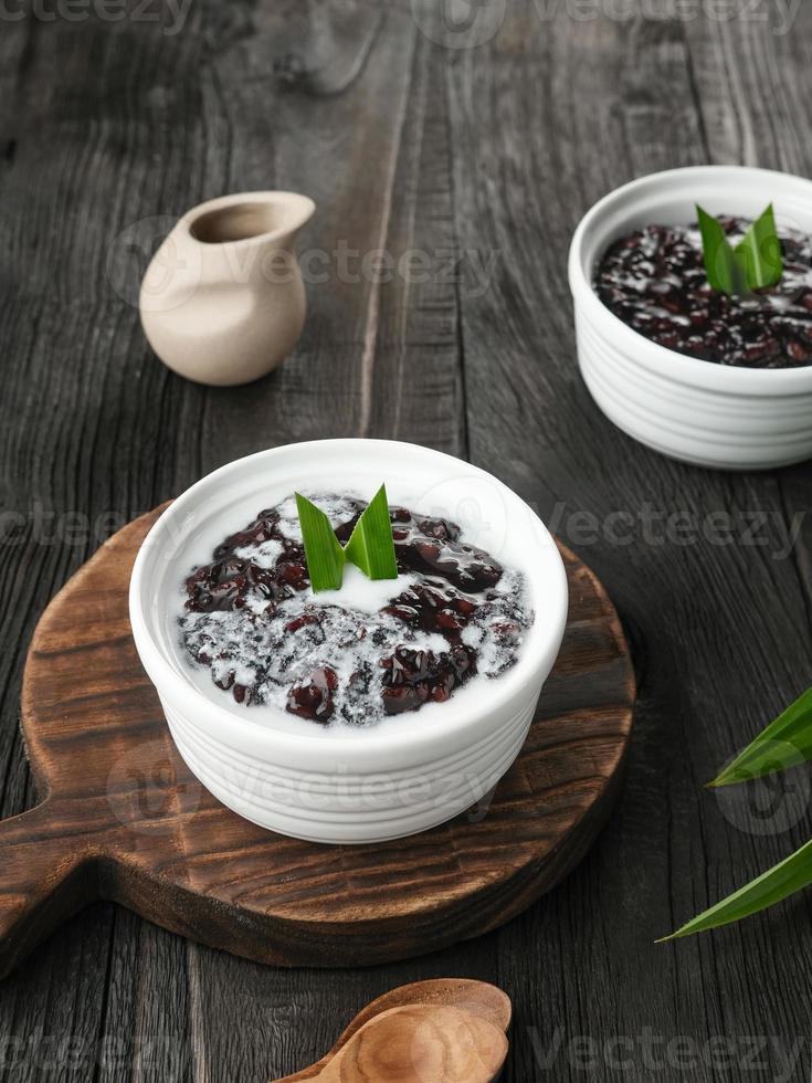 Bubur Ketan Hitam, Indonesian dessert. Black glutinous rice porridge with coconut milk, sugar and pandan leaf. Served in a white bowl on a wooden table. photo